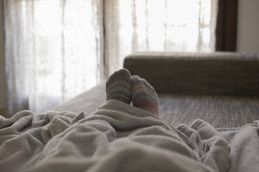 Low Section Of Person Wearing Socks Relaxing On Bed At Home - EYF08982