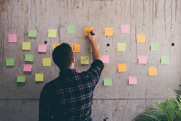 Rear View Of Man Writing On Adhesive Note In Office - EYF08994