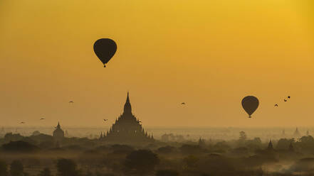 Myanmar, Region Mandalay, Bagan, Silhouetten von Heißluftballons, die in der nebligen Morgendämmerung über alten Tempeln fliegen - TOVF00203