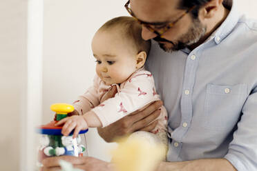Father holding baby girl playing with toy - SODF00796