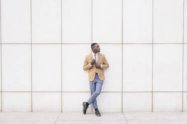 Young businessman leaning against a wall looking sideways - ABZF03212