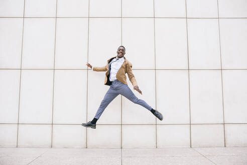 Young businessman jumping in front of a wall - ABZF03214