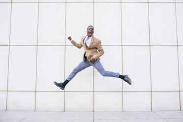 Young businessman jumping and shouting in front of a wall - ABZF03215