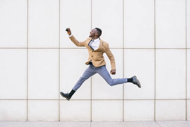 Young businessman jumping and taking a selfie in front of a wall - ABZF03219
