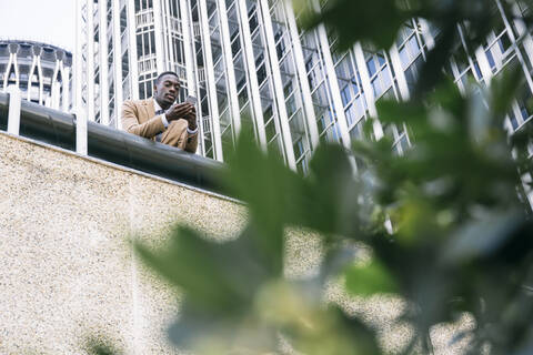 Junger Geschäftsmann lehnt an einem Geländer in der Stadt und benutzt ein Smartphone, lizenzfreies Stockfoto