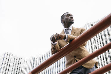 Young businessman leaning on a railing in the city looking away - ABZF03231