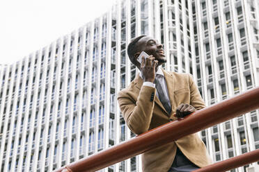 Young businessman leaning on a railing in the city talking on the phone - ABZF03232