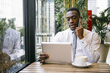 Junger Geschäftsmann mit Tablet und Smartphone in einem Café - ABZF03236