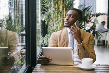 Young businessman using tablet and smartphone in a cafe - ABZF03237