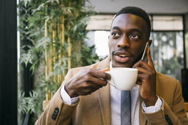 Junger Geschäftsmann trinkt eine Tasse Kaffee und telefoniert in einem Cafe - ABZF03239