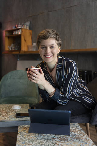 Portrait of smiling freelancer sitting in a coffee shop with digital tablet and smartphone stock photo