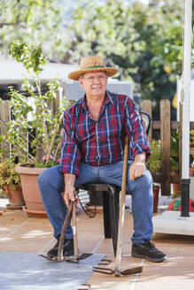 Älterer Mann mit Gartengeräten auf einem Stuhl sitzend - LJF01596