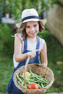 Smiling girl with basket and fresh fruit and vegetables in garden - LJF01623