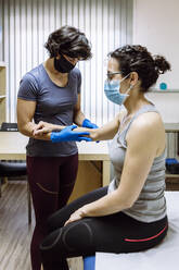 Female physiotherapist with mask treating female client on ellbow - XLGF00291