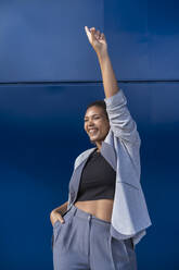 Lächelnde Geschäftsfrau mit erhobenem Arm vor einer blauen Wand - SNF00434