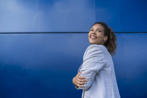 Smiling businesswoman with crossed arms in front of blue wall stock photo