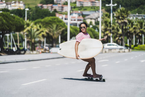 Female skateboarder with surfboard on street - MTBF00500
