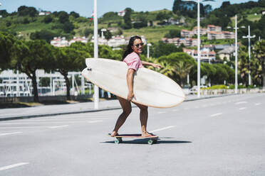 Female skateboarder with surfboard on street - MTBF00501