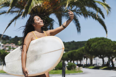 Weibliche Surferin mit Surfbrett macht ein Selfie mit ihrem Smartphone - MTBF00503