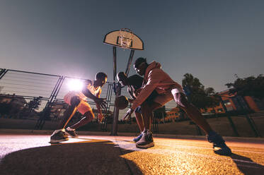 Männliche Freunde spielen nachts am Wochenende Basketball im Hof - OCMF01395