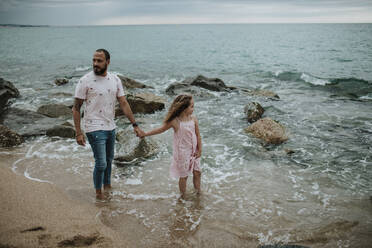 Vater und Tochter halten sich am Strand an den Händen - GMLF00319