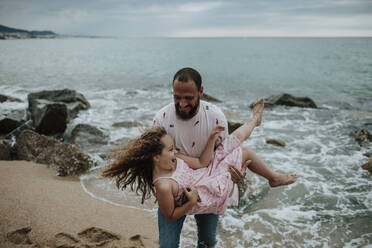 Smiling father carrying daughter at beach - GMLF00322