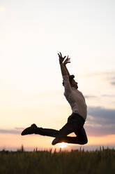 Mann tanzt bei Sonnenuntergang auf einem Feld - MAUF03476