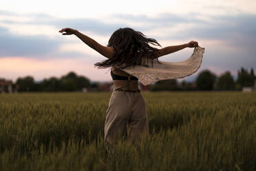 Frau tanzt auf einem Feld im Abendlicht - MAUF03478