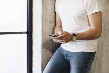 Älterer Mann steht am Fenster und benutzt ein Smartphone - DGOF01092