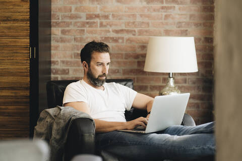 Älterer Mann sitzt im Sessel und benutzt einen Laptop, lizenzfreies Stockfoto