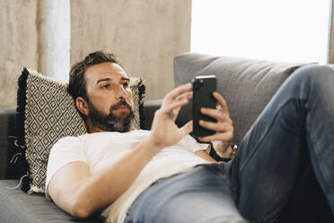 Mature man lying on couch, using smartphone - DGOF01096