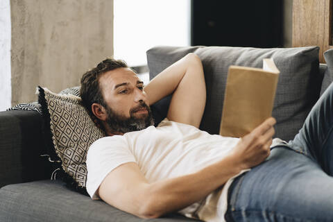 Älterer Mann liegt auf der Couch und liest ein Buch, lizenzfreies Stockfoto