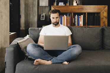 Mature man sitting on couch, using laptop - DGOF01100
