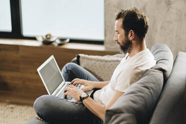 Mature man sitting on couch, using laptop - DGOF01101