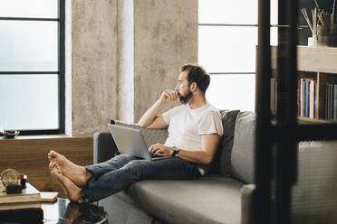 Mature man sitting on couch, using laptop, thinking - DGOF01102