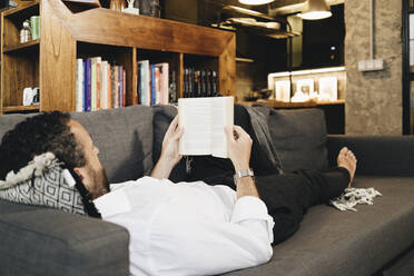 Mature man lying on couch, relaxing, reading book - DGOF01134