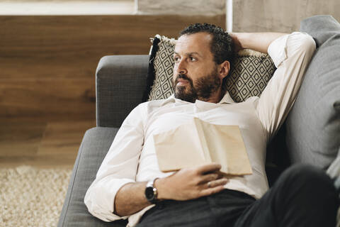 Älterer Mann liegt auf der Couch, entspannt, liest ein Buch, lizenzfreies Stockfoto