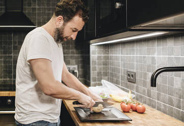 Mature man standing in kitchen, chopping onions - DGOF01143