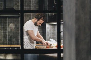 Mature man standing in kitchen, slicing tomatoes - DGOF01146