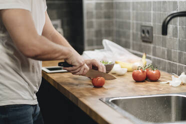 Älterer Mann steht in der Küche und schneidet Tomaten - DGOF01147