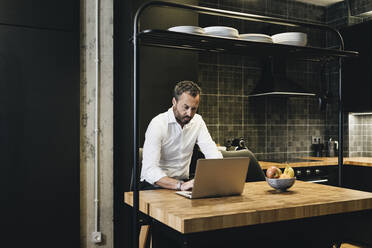 Älterer Geschäftsmann bei der Arbeit in der Küche, mit Laptop - DGOF01165