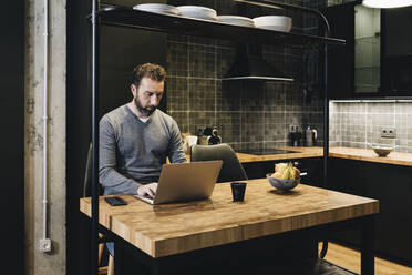 Älterer Geschäftsmann bei der Arbeit in der Küche, mit Laptop - DGOF01175