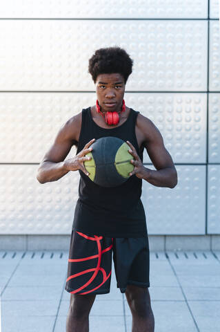 Porträt eines jungen Mannes mit Kopfhörern, der einen Basketball hält, lizenzfreies Stockfoto