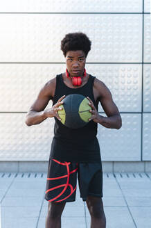 Porträt eines jungen Mannes mit Kopfhörern, der einen Basketball hält - JMPF00016