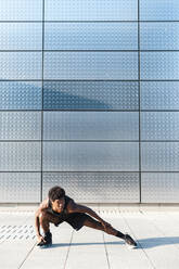 Young man stretching at a metallic shining wall - JMPF00020