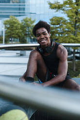 Portrait of a smiling young man with headphones sitting in the city - JMPF00039