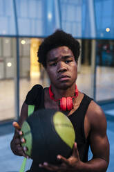 Porträt eines selbstbewussten jungen Mannes mit Kopfhörern und Basketball in der Stadt - JMPF00040
