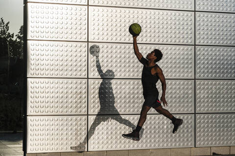 Junger Mann spielt Basketball an einer metallisch glänzenden Wand, lizenzfreies Stockfoto