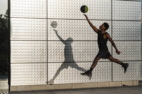 Junger Mann spielt Basketball an einer metallisch glänzenden Wand, lizenzfreies Stockfoto