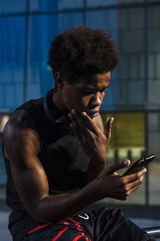 Junger Mann singt Smartphone in der Abenddämmerung in der Stadt, lizenzfreies Stockfoto